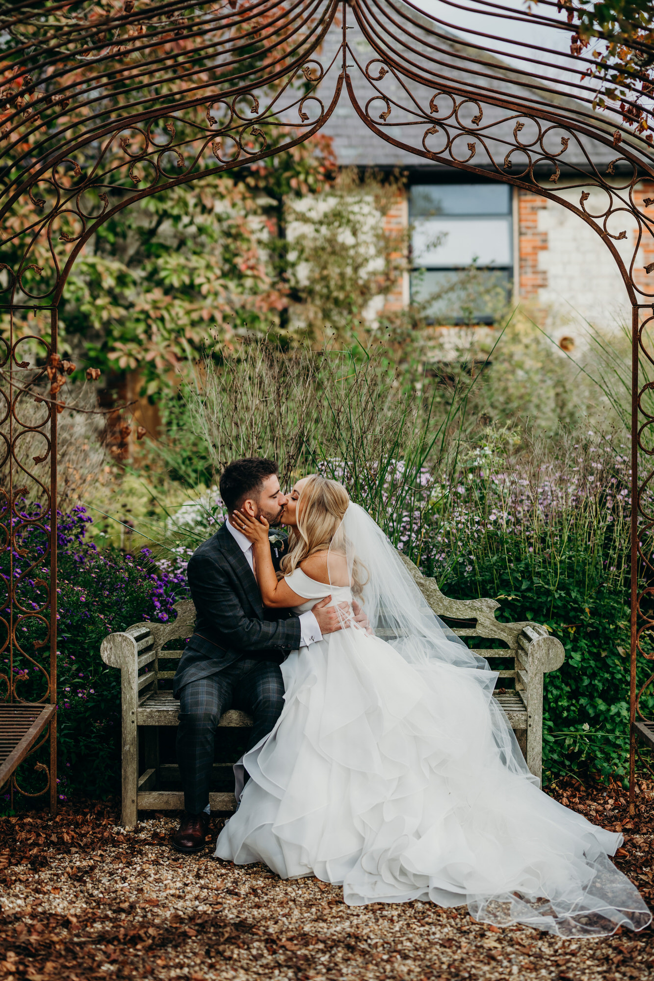 Newlyweds kiss on bench amongst the Autumn colours at Bury Court 