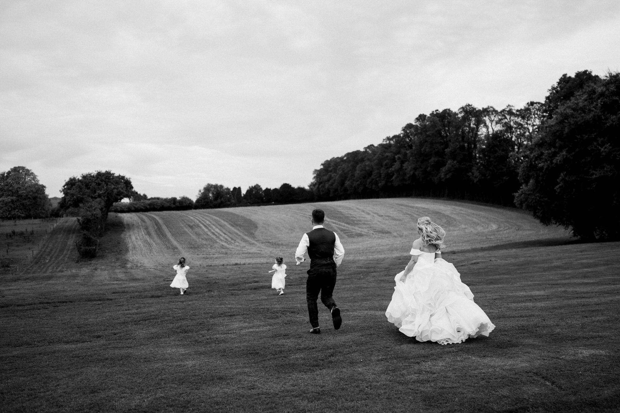 Bride and groom chase their twin girls across field at Bury Court